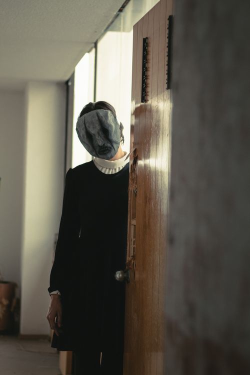 Free Mysterious woman with obscured face standing in quiet hallway, creating a surreal and eerie atmosphere. Stock Photo