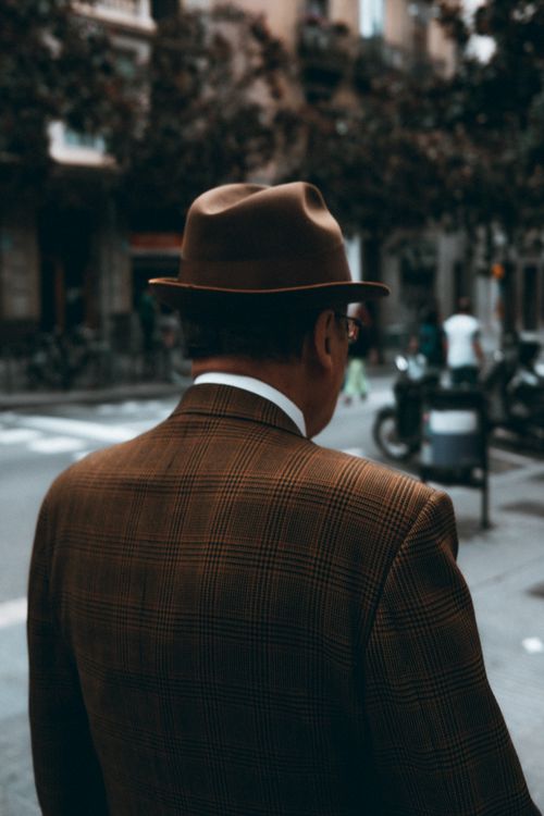 Free Man in brown plaid suit walking in urban street with blurred background and classic hat. Stock Photo