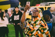 一名身着彩色服装的女子在户外聚会上自拍，背景是人群