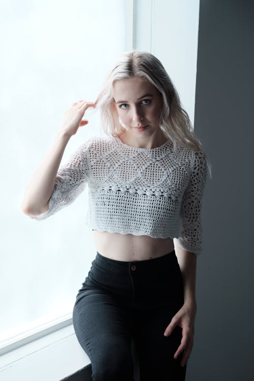 Blond Woman Wearing a Lace Blouse Sitting on a Windowsill