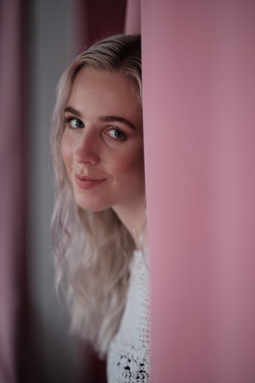 Free Close-up portrait of a smiling woman with long blonde hair behind a pink curtain. Stock Photo