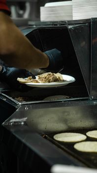 Chef preparing tacos with tortillas on a grill in a professional kitchen setting.