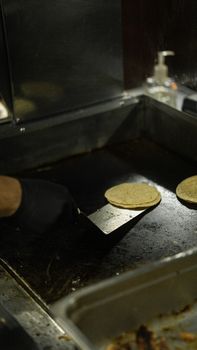 Hand turning corn tortillas on a hot grill with a spatula, close-up