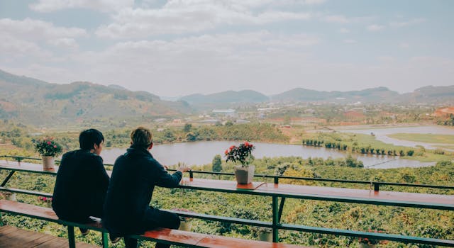 两个人坐在长凳上，俯瞰着田野和湖泊，欣赏着风景优美的乡村景观