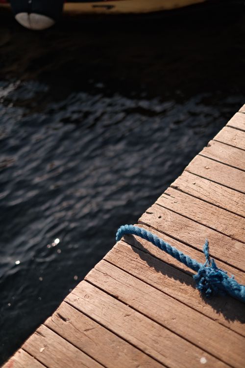 Free A close-up of a wooden dock with blue rope overlooking calm waters, capturing tranquility. Stock Photo