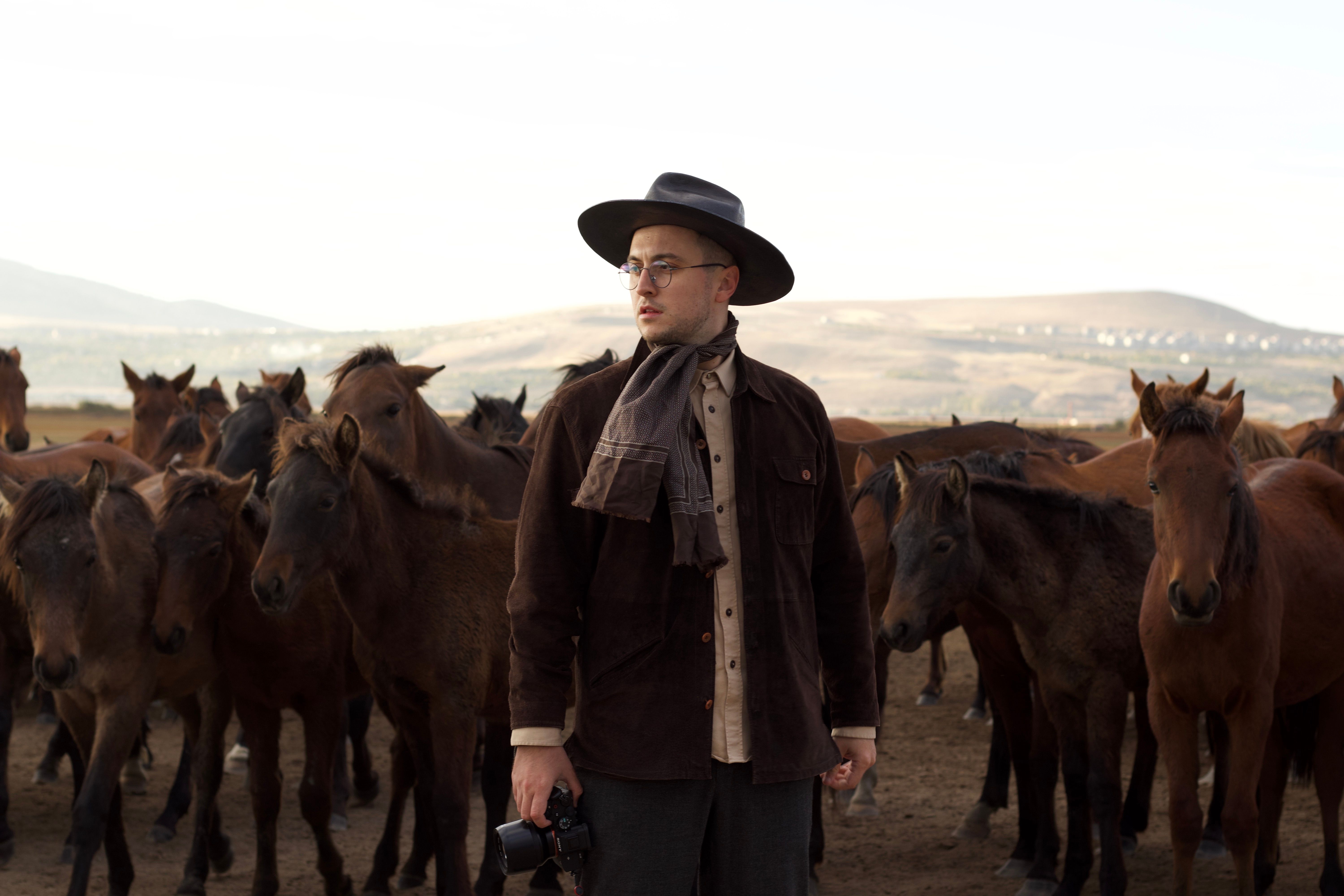 A in Brown Jacket with Black Hat Standing Beside Brown Horses · Free Stock Photo