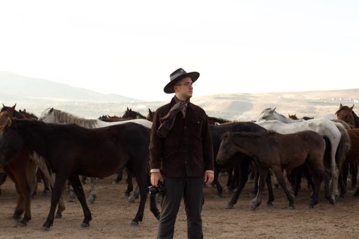 A man with a camera stands among a herd of wild horses in a vast, open landscape.