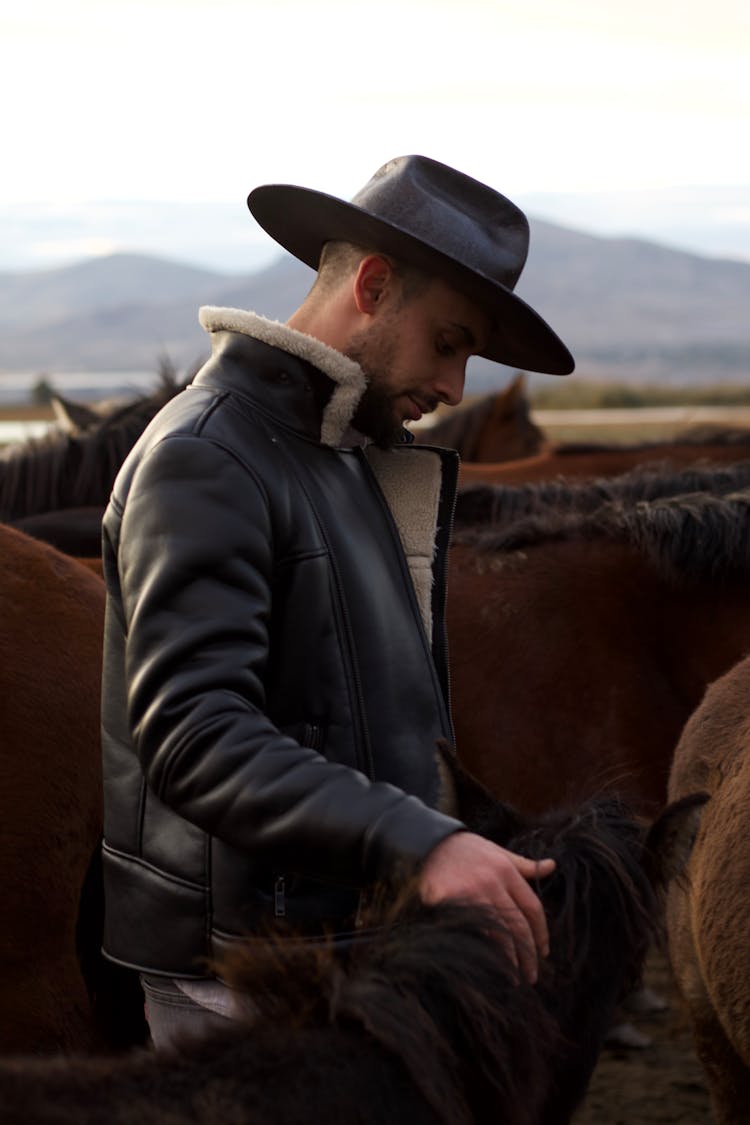 Man In Hat And Jacket Among Horses