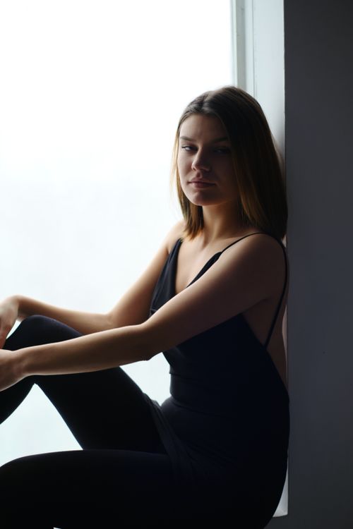 Free Silhouette of a woman sitting by a window, dressed in black, in a serene indoor setting. Stock Photo