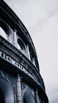 Dramatic upward angle of Rome's iconic Colosseum against a cloudy sky, showcasing ancient architecture.