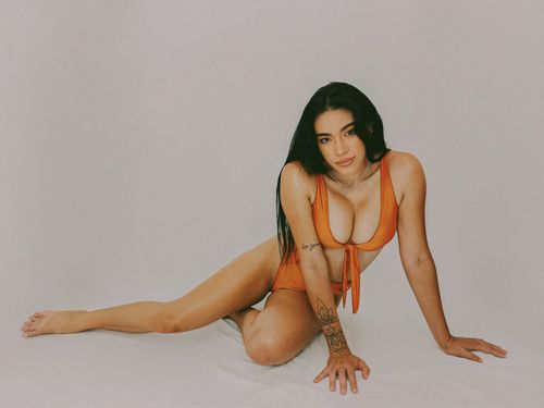 Free Woman posing in orange swimsuit on a light background, showcasing tattoos and fashion style. Stock Photo