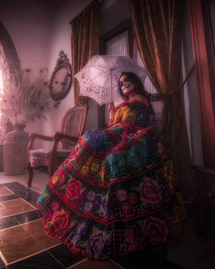 A Woman In Printed Dress Holding An Umbrella While Sitting On A Wooden Chair