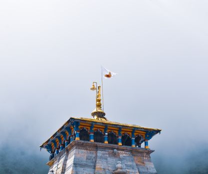 A striking temple tower with a golden spire and flag amidst a misty background, showcasing traditional architecture.