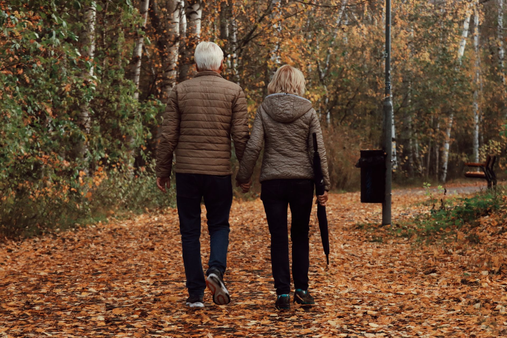 An older person walking on a park trail in autumn