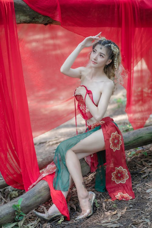 A Woman in Red Crop Top Sitting on Wood Log