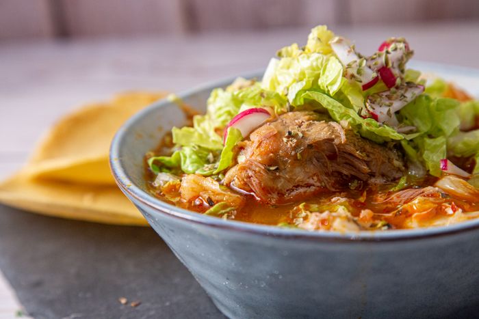 Pozole rojo servido con guarniciones frescas