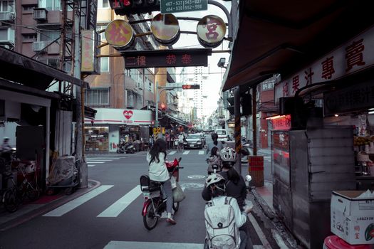 Vibrant urban street in Asia with cyclists navigating through bustling shops and signage.