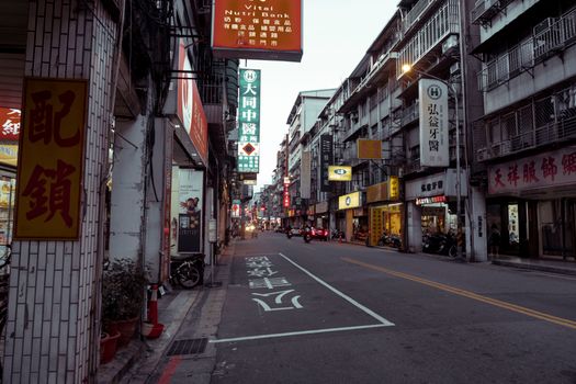 A lively city street lined with shops and signs glowing in the evening light.