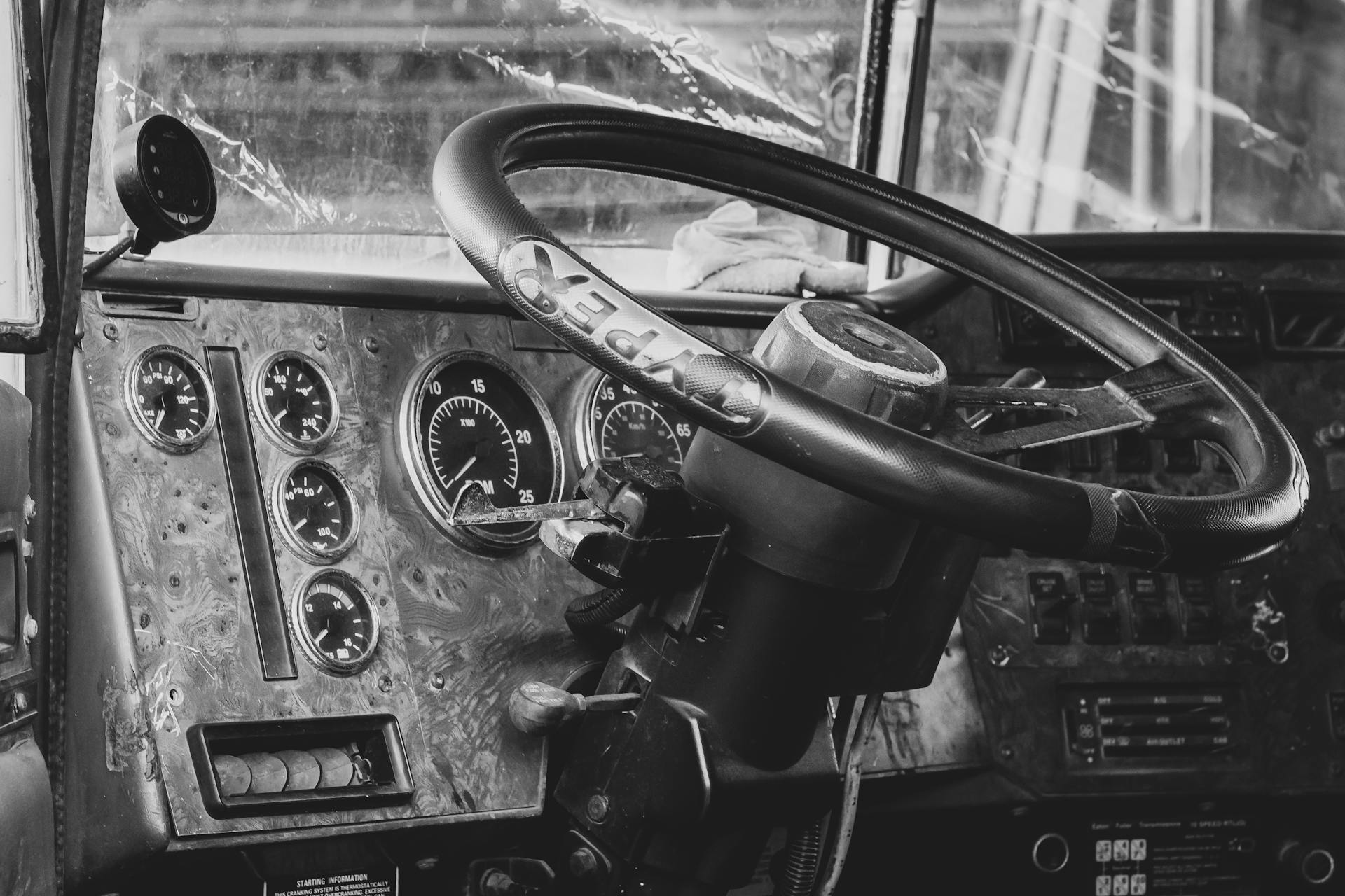 Close-up of an old truck dashboard in black and white, showcasing gauges and steering wheel.