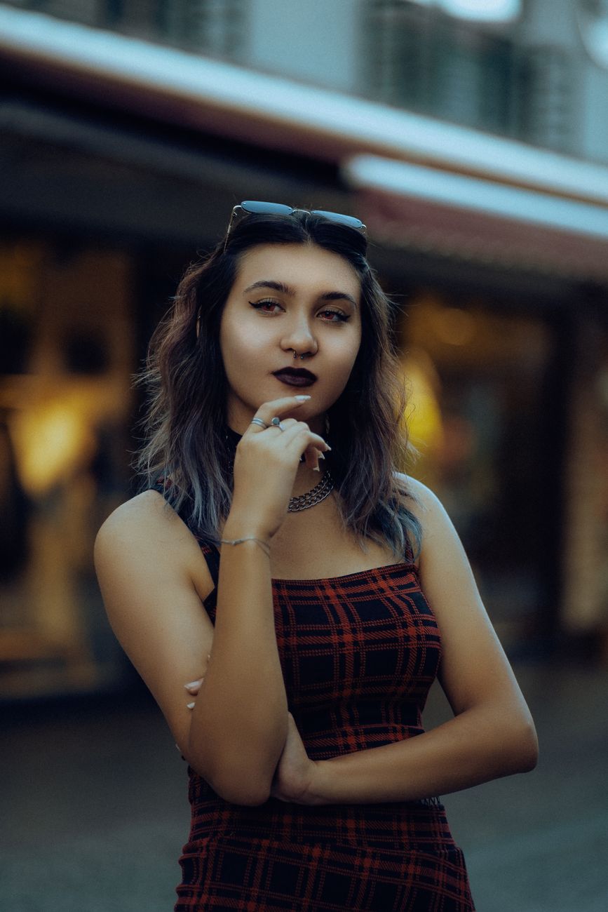 Confident woman posing in a plaid dress with sunglasses on head, embracing a stylish urban vibe.