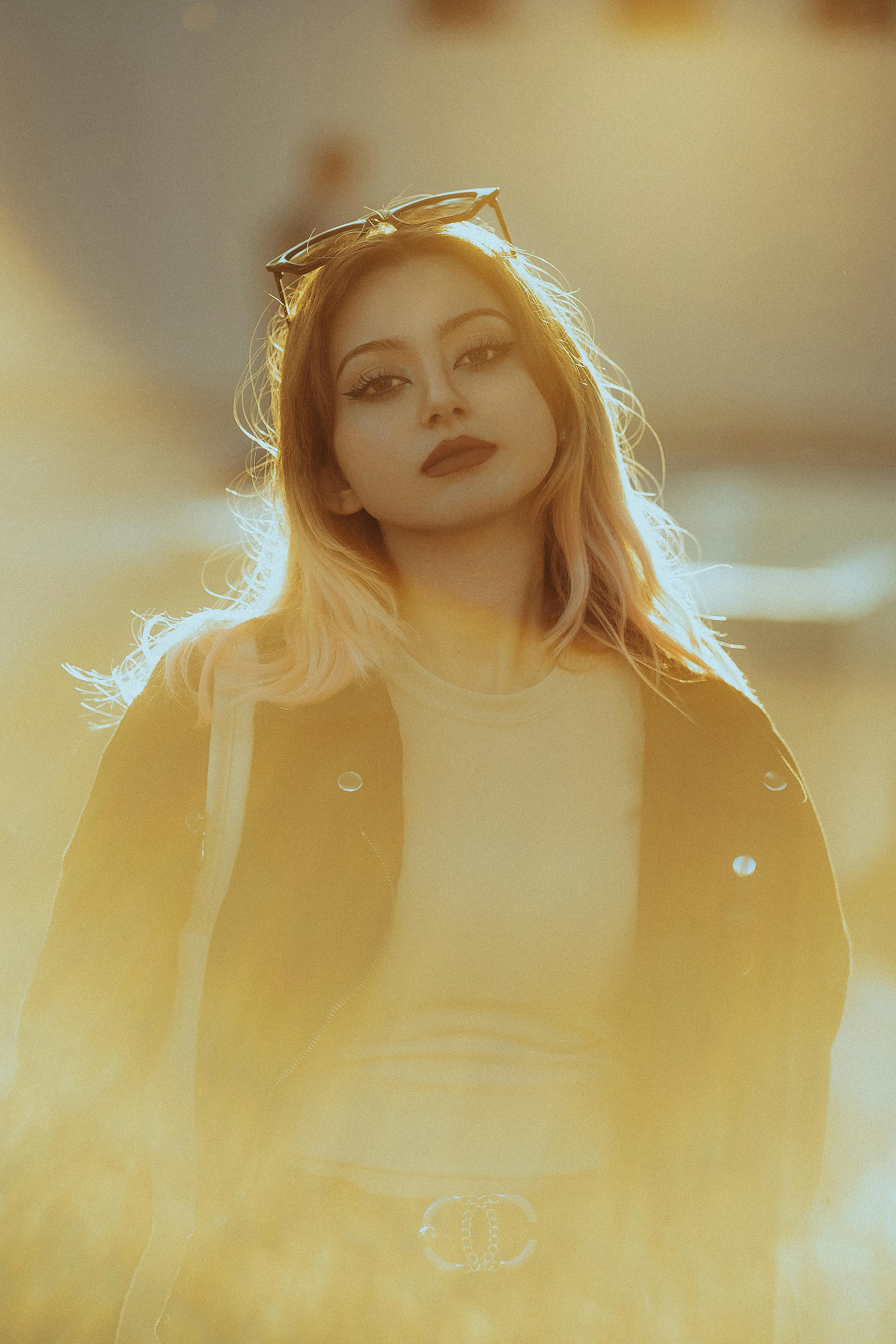 Portrait of a fashionable woman with sunglasses posing gracefully under golden sunlight.