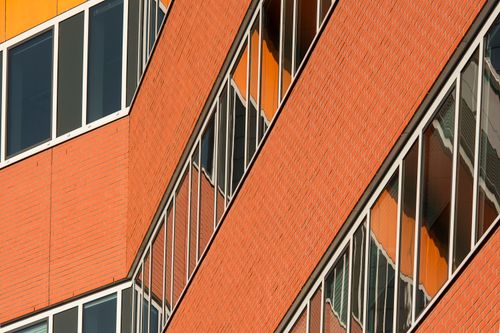 Free Close-up of modern architectural facade with orange brickwork and reflective windows. Stock Photo