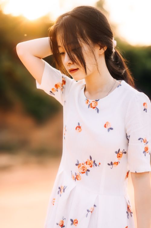 Free Young Asian woman in floral dress with long hair poses outdoors at sunset. Stock Photo