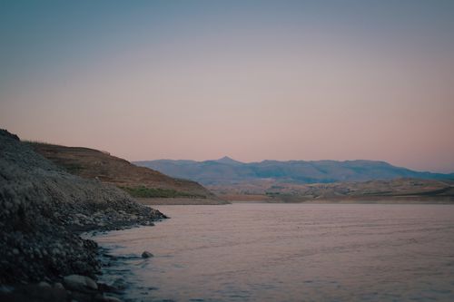 Free Peaceful view of rocky shoreline and distant mountains at sunrise. Stock Photo