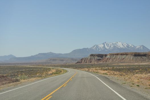 Wide open road in Hanksville, Utah with stunning desert views and snowcapped mountains.