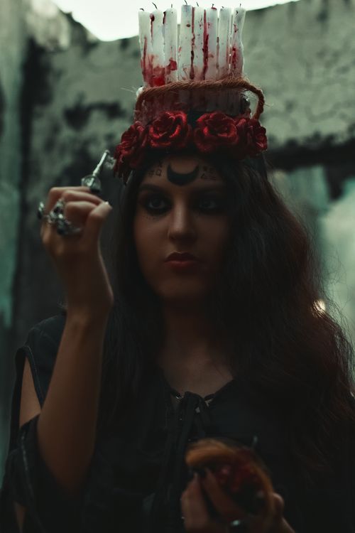 Free Young woman in a dark, eerie Halloween costume holding ceremonial objects. Perfect for horror themes. Stock Photo