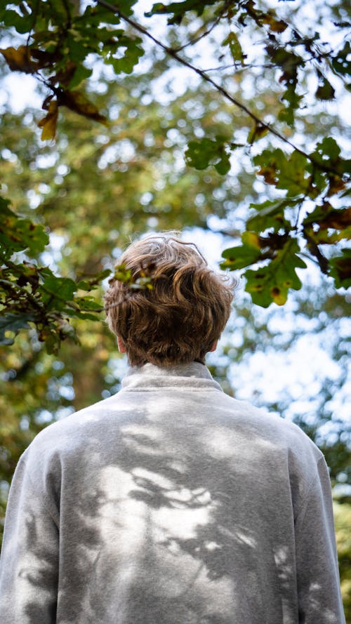 A Back View of a Man in White Long Sleeves Standing Under the Tree