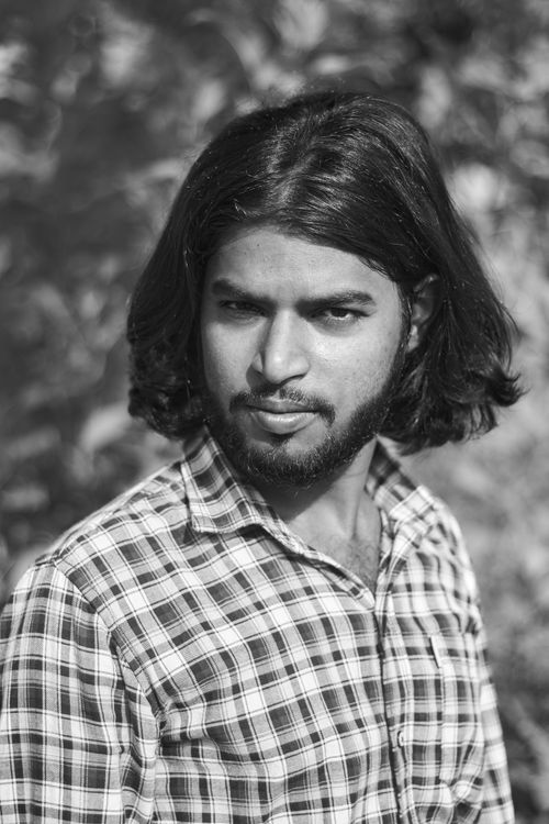 Free Black and white portrait of a young man with long hair, wearing a plaid shirt outdoors. Stock Photo