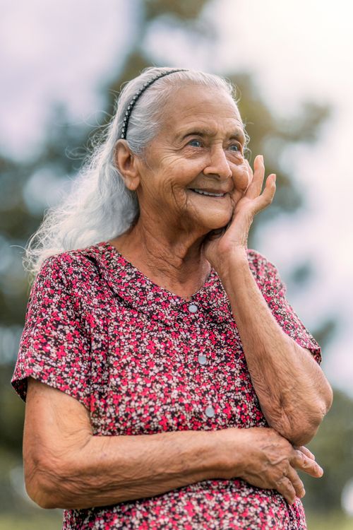 Free Charming portrait of a happy senior woman in a floral dress enjoying the sunny outdoors. Stock Photo