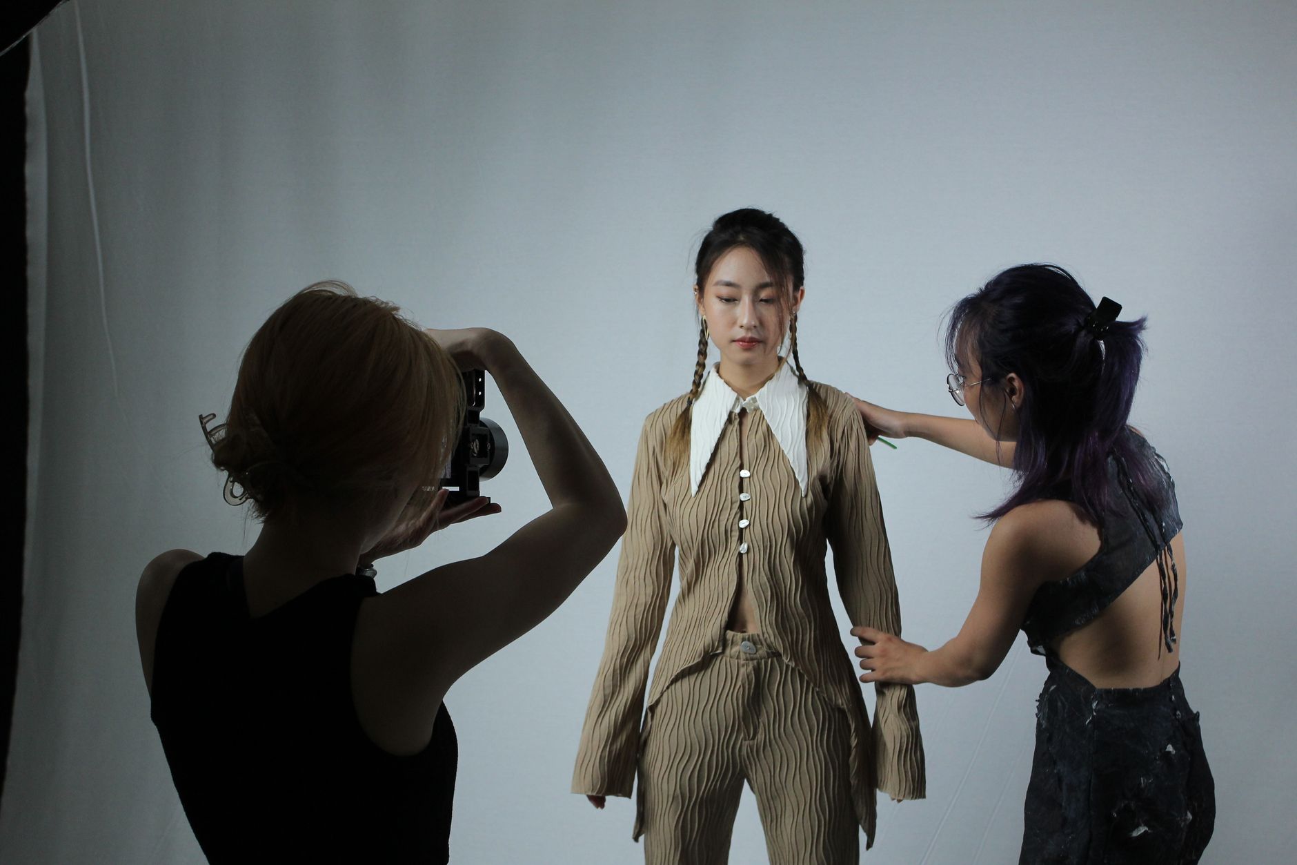 Model preparing for a fashion photoshoot with assistance and photographer.