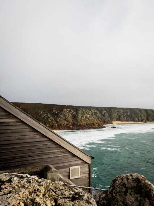 Free Scenic view of Porthcurno's coastline with a rocky shoreline and overcast sky. Stock Photo