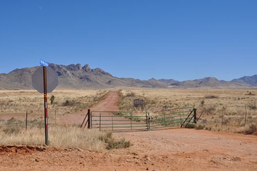 Dirt road leading to mountains in Valentine, TX, USA with a fence and clear blue sky.