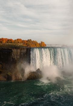 Capture of Niagara Falls' majestic flow over cliffs during fall with vibrant foliage.