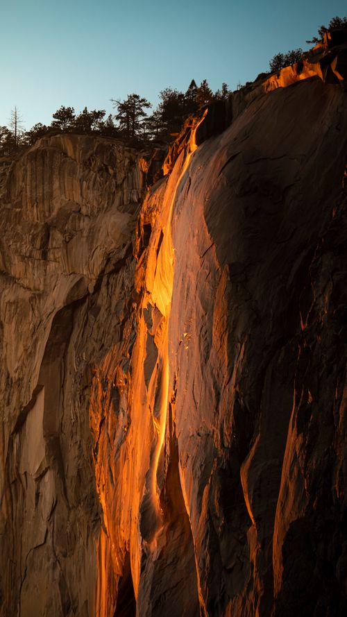 Free Golden sunset light casts a dramatic glow on a rugged mountain cliff. Ideal for nature and scenery lovers. Stock Photo