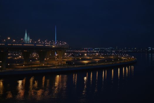 A beautifully lit urban bridge at night reflecting in calm waters, showcasing modern architecture.