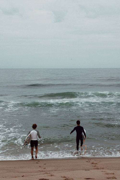 Free Two surfers with surfboards walking towards the ocean, preparing to surf at the beach. Stock Photo