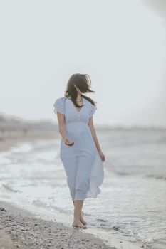 A woman in a white dress walking along a serene beach at sunrise.