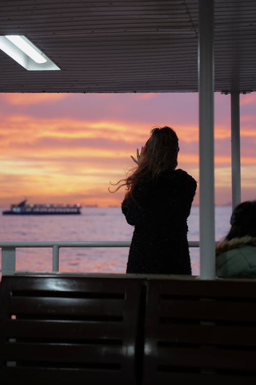 Back View of a Woman Looking at Body of Water at Sunset