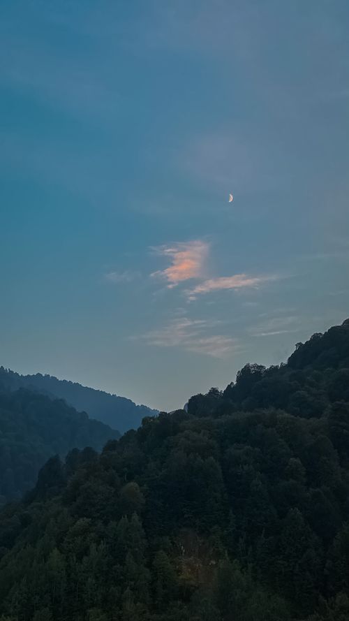 Free Breathtaking view of hills and a crescent moon in the clear sky during twilight. Stock Photo