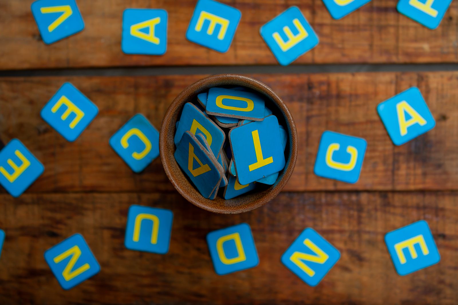 Blue alphabet tiles in a small bowl and scattered across a wooden table