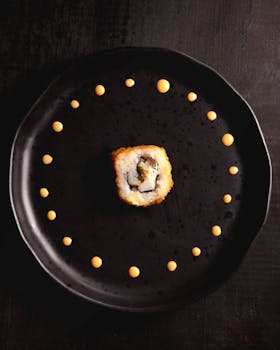 A beautifully arranged sushi roll with a circular pattern of sauce on a black plate. Ideal for food and culinary visuals.