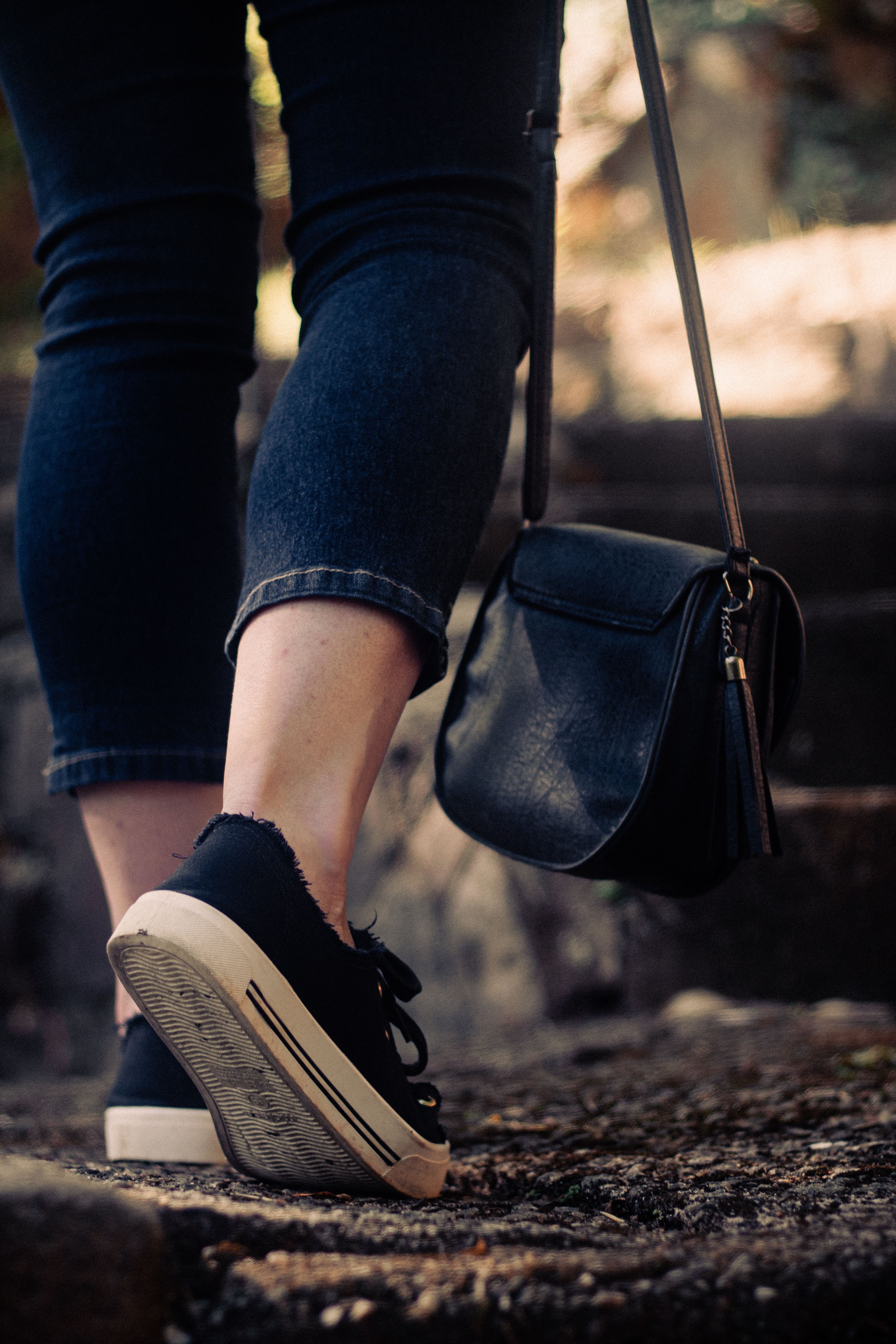 A stylish urban close-up of a person walking with a handbag and jeans.