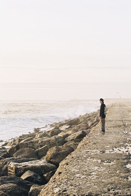 A solitary man stands on a rocky shoreline in Figueira da Foz, Portugal, gazing at the ocean.