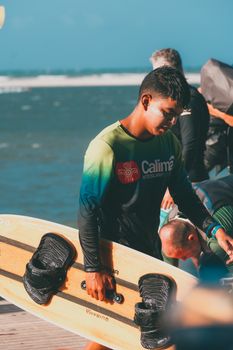 A surfer in vibrant sportswear holding a surfboard near the ocean on a sunny day.