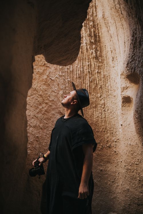 Free A photographer in a black hat and shirt explores a dramatic cave with rock formations. Stock Photo