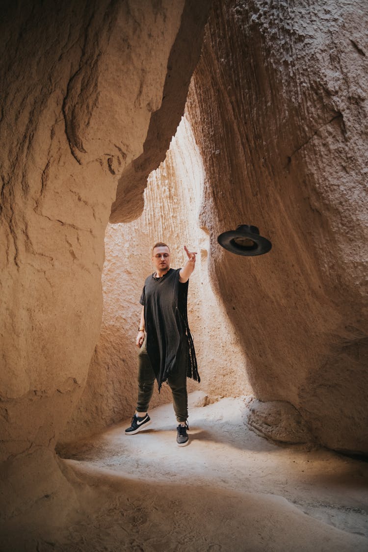 A Man In Black Outfit Throwing A Black Hat Inside A Cave